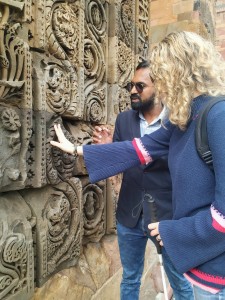 My guide and I are standing in front of wall with lots of carvings. I am exploring the carvings with my right hand while holding my cane with my left