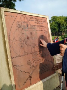 An upright brown tactile map of  Qutub MInar. my right hand is exploring one of the lines on the map. 